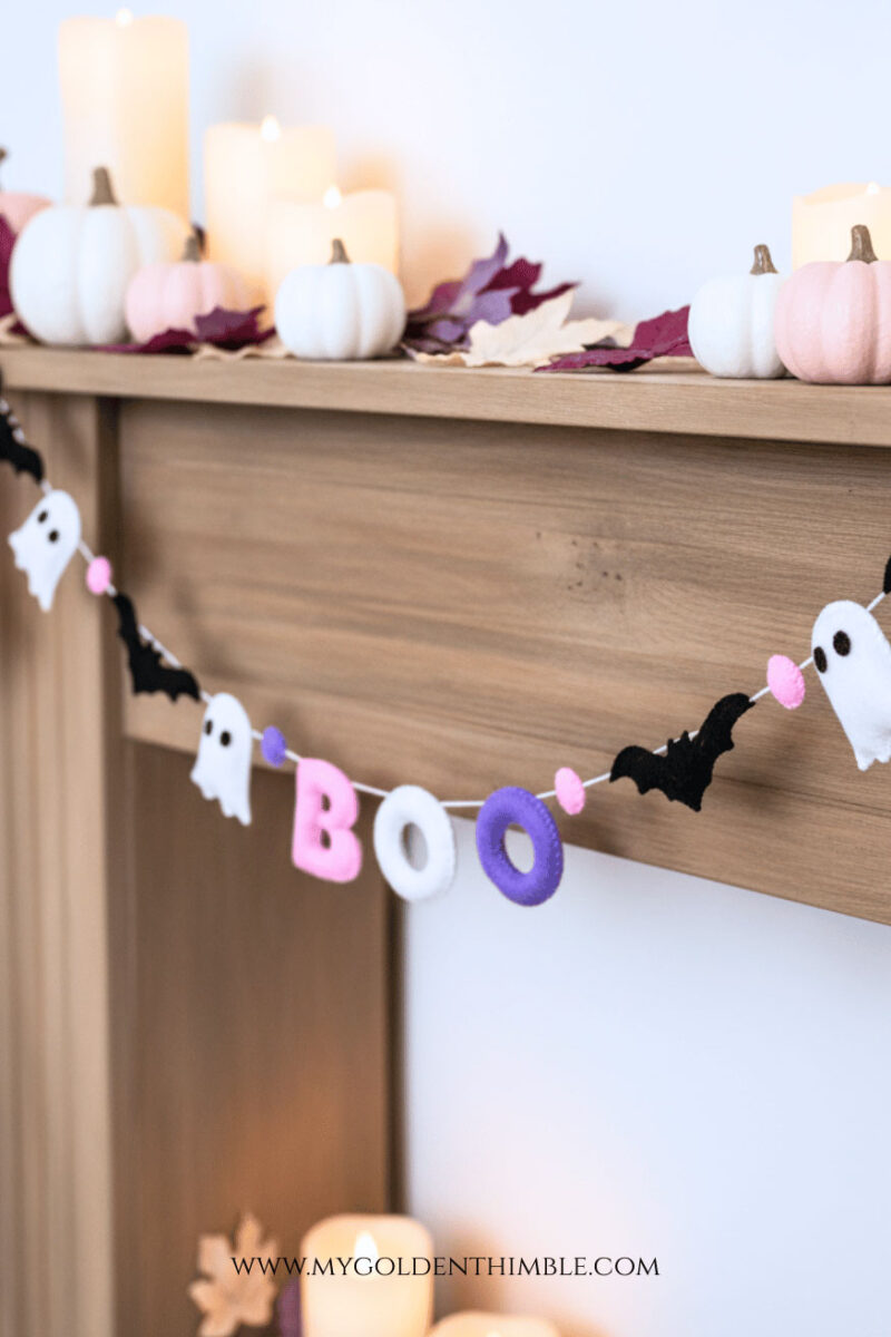 DIY Halloween garland with Boo felt letters, happy ghosts, and bats hanging on a wall, colorful Halloween décor for home.