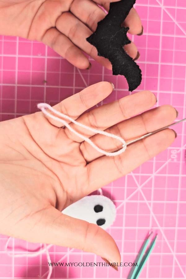 Assembling DIY Halloween garland, threading pink and purple felt letters, ghosts, and bats onto cord for hanging.