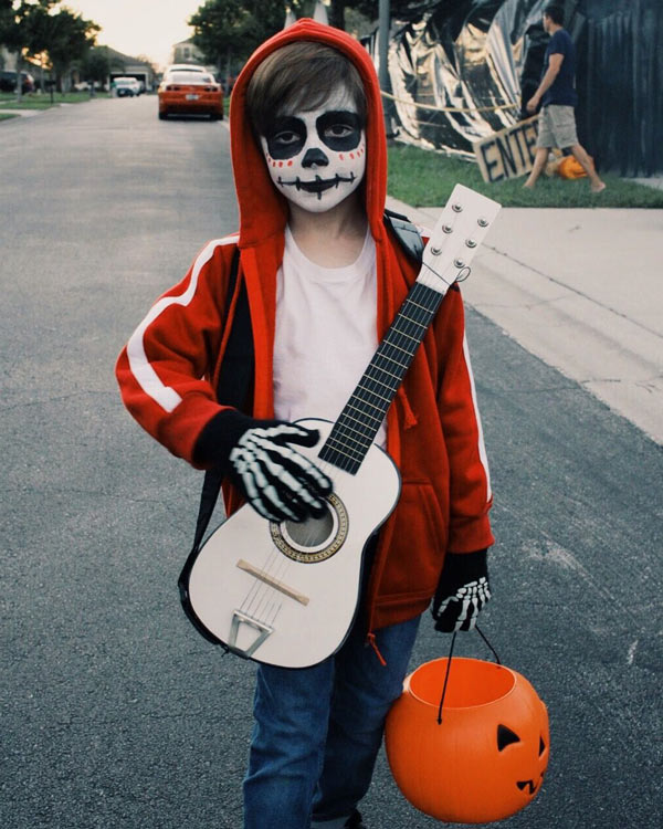 small kid dress as miguel from coco with a red hoodie and a toy guitar