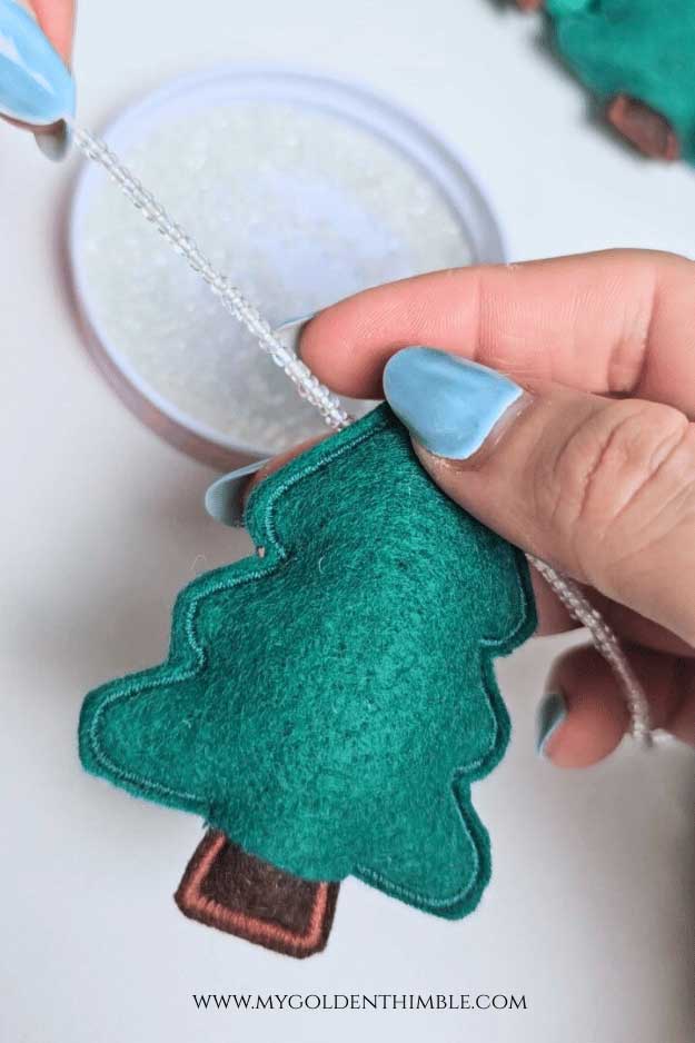 Stringing embroidered felt trees and beads together to create a Felt Christmas Garland DIY.