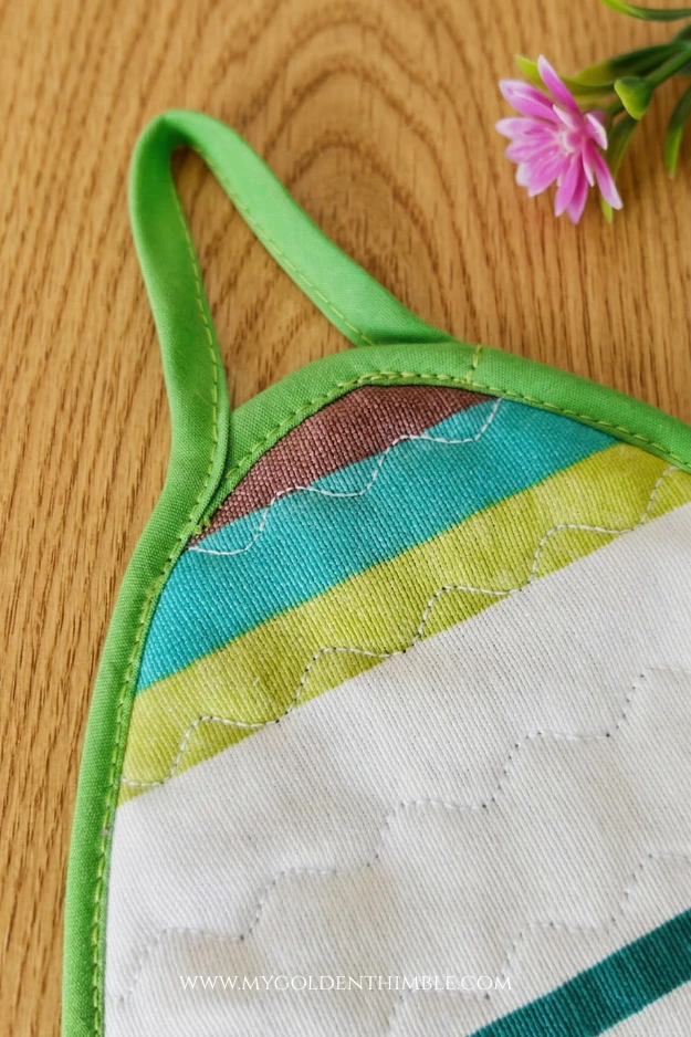 Finished Easter egg potholder made with cotton fabric and decorative stitching displayed on a rustic wooden kitchen table