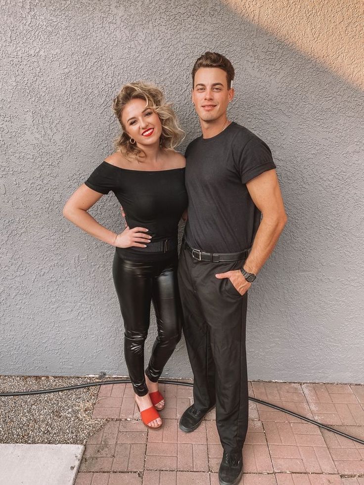 Two people standing side by side against a textured gray wall. The person on the left is wearing an off-the-shoulder black top and black pants, with red shoes. Halloween costumes diy couples, Cute couple halloween costumes
