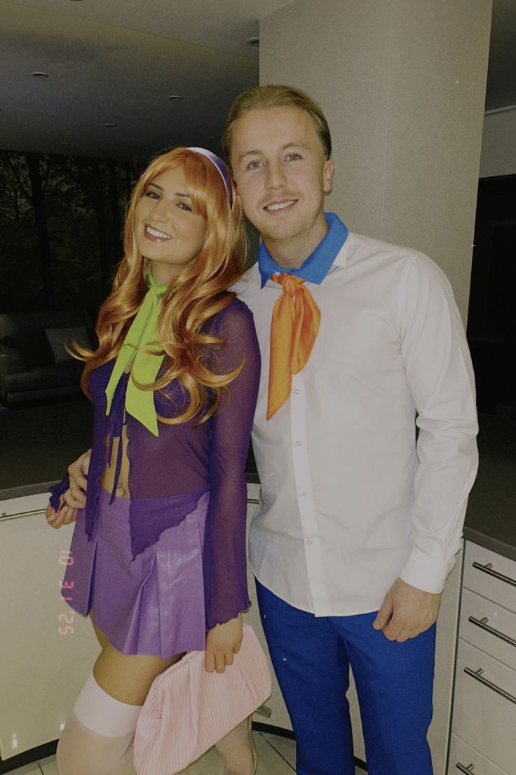 Two people dressed in costumes. The person on the left is wearing a purple outfit with a green bow and has long, red hair. Costume ideas, Halloween outfits