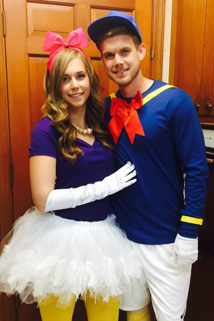 Two people dressed in costumes. The person on the left is wearing a blue top, white gloves, and a pink bow headband, while the person on the right is dressed in a blue shirt with a red bow tie, white pants, and a blue cap.