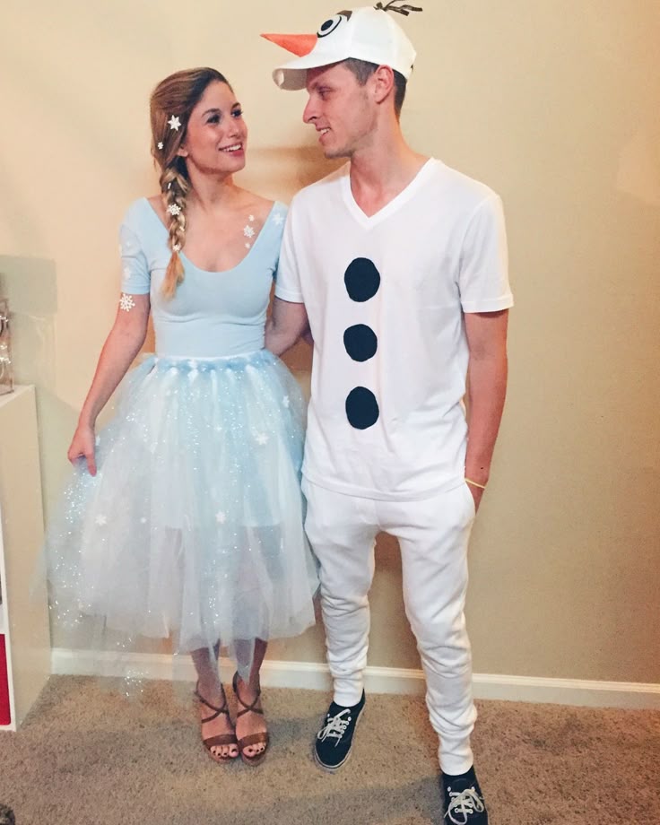 Two people dressed in costumes. The person on the left is wearing a light blue dress with a tulle skirt and has a braid adorned with small white flowers.