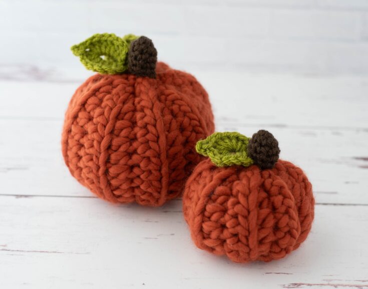 Two chunky orange crochet pumpkins with green stems