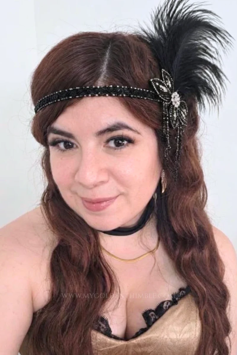 Close-up of a woman wearing a gold satin corset, black choker, and a feathered hair accessory.