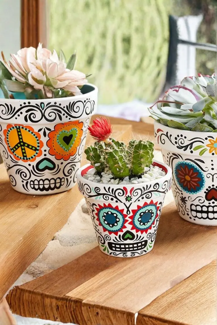 Terracotta planter pots painted with sugar skull designs holding small succulent plants.