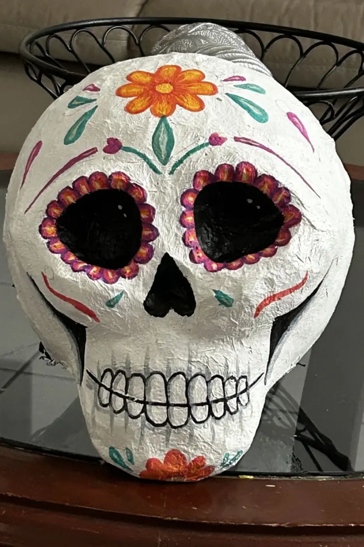 White papier-mâché sugar skull mask decorated with orange floral accents.