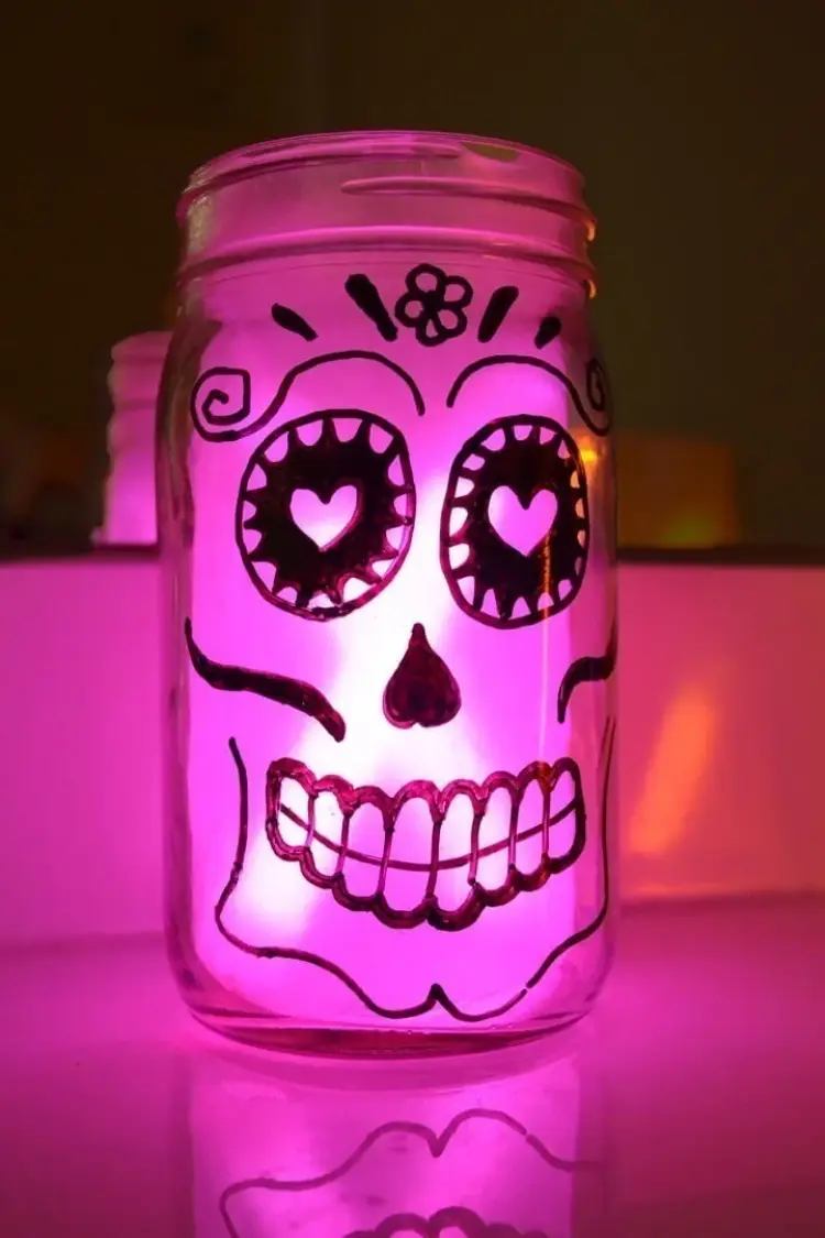 DIY pink illuminated glass mason jar painted with a glowing sugar skull face for Day of the Dead.