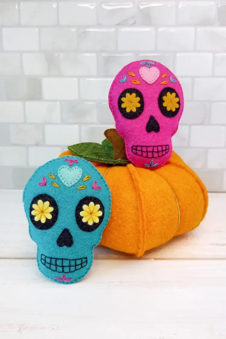 Two small felt decorative sugar skulls sitting next to a faux pumpkin.