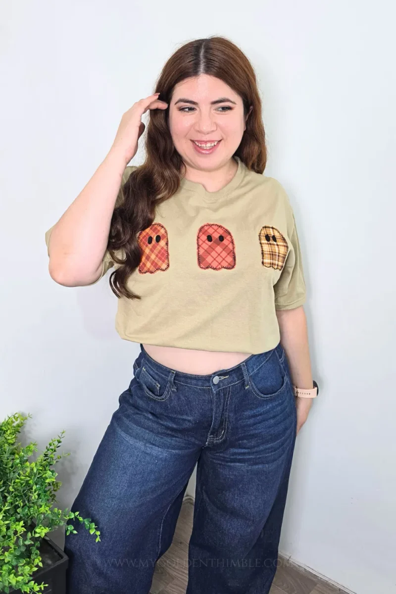 Woman posing with one hand near her head, wearing the handmade autumn ghost applique t-shirt and jeans.