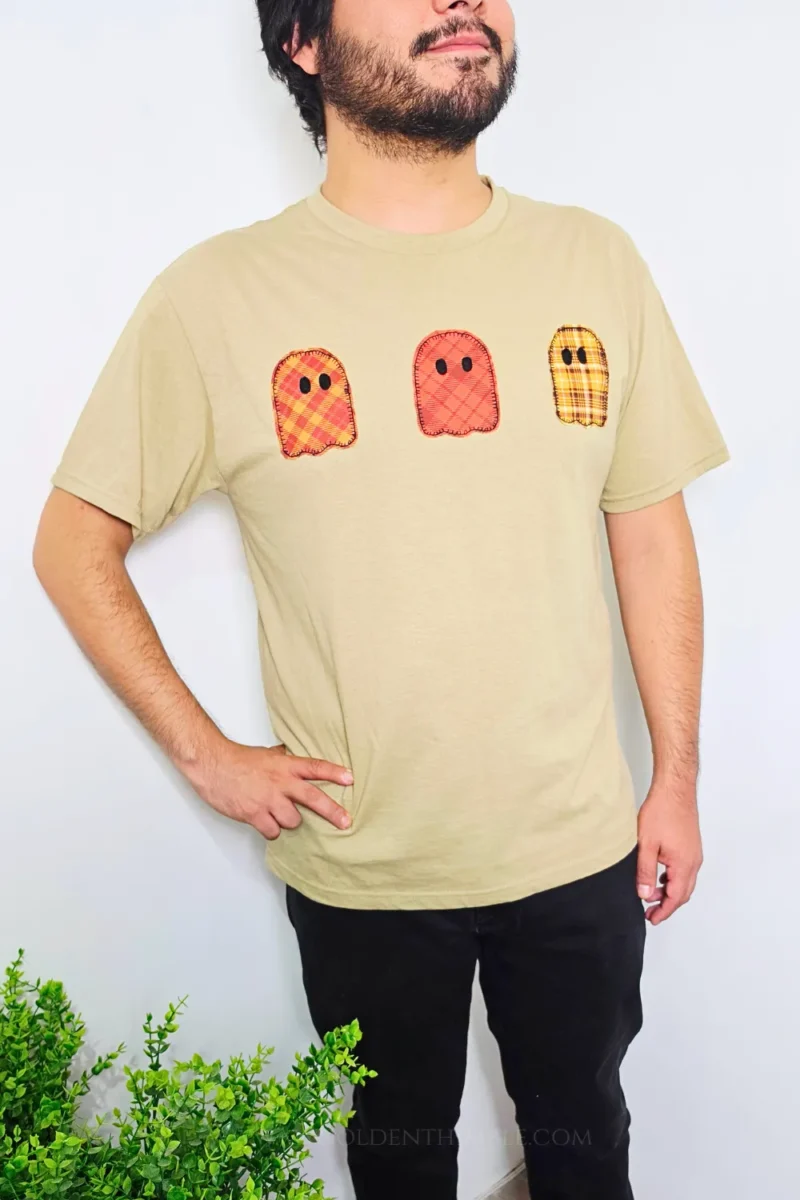 Man wearing the beige t-shirt featuring three colorful plaid ghost appliques across the chest.
