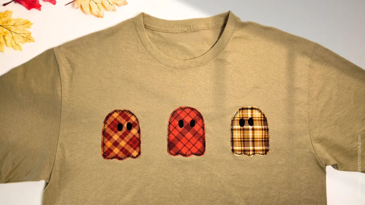 Flat-lay close-up showing the row of three distinct plaid ghost appliques stitched across the beige t-shirt.