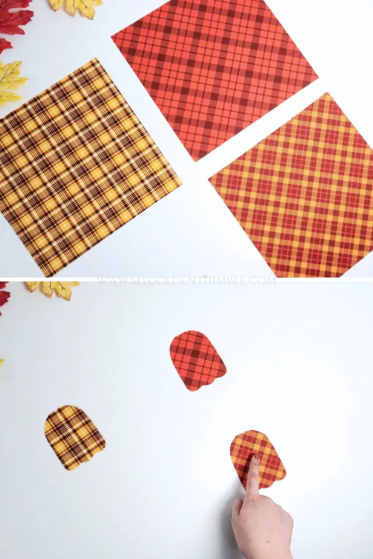 Hands positioning small ghost-shaped fabric cutouts onto plaid fabrics on a white cutting mat.