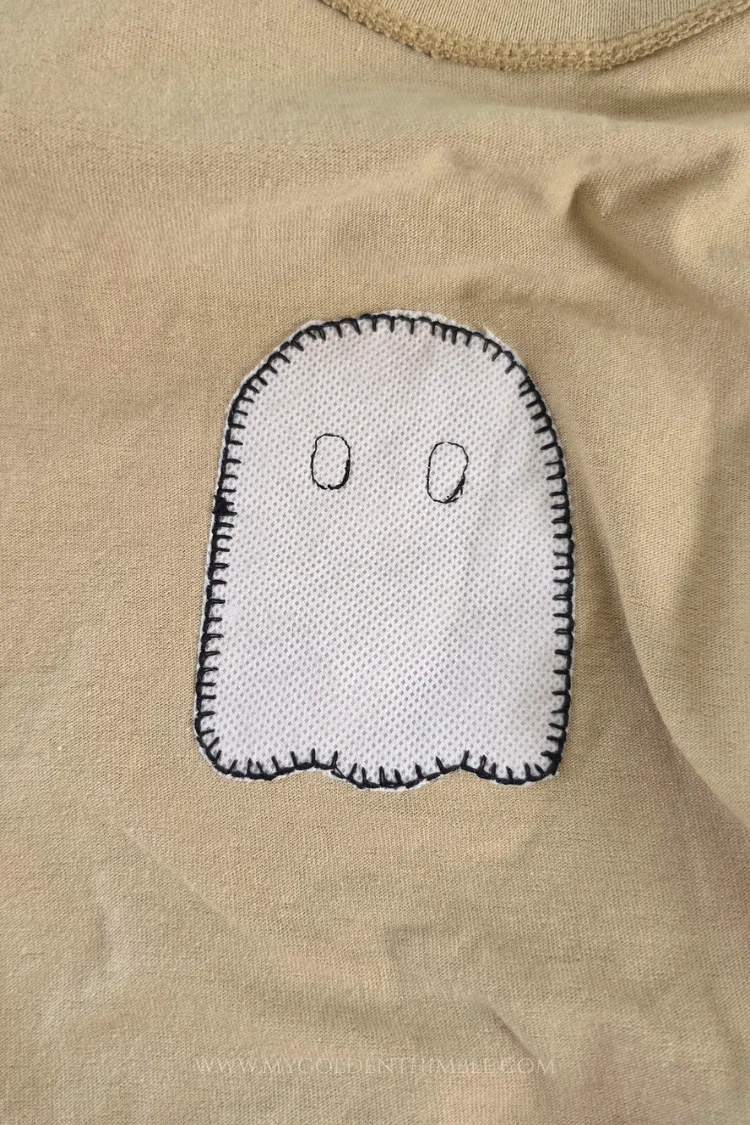 Close-up top-down view of a completed white stabilizer ghost applique stitched onto a beige t-shirt.