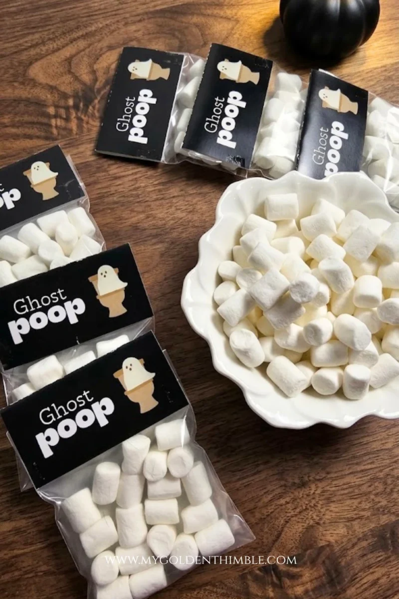 High-angle shot of 'Ghost Poop' treat bags neatly arranged on a rich walnut wooden tabletop alongside a small white bowl of marshmallows.